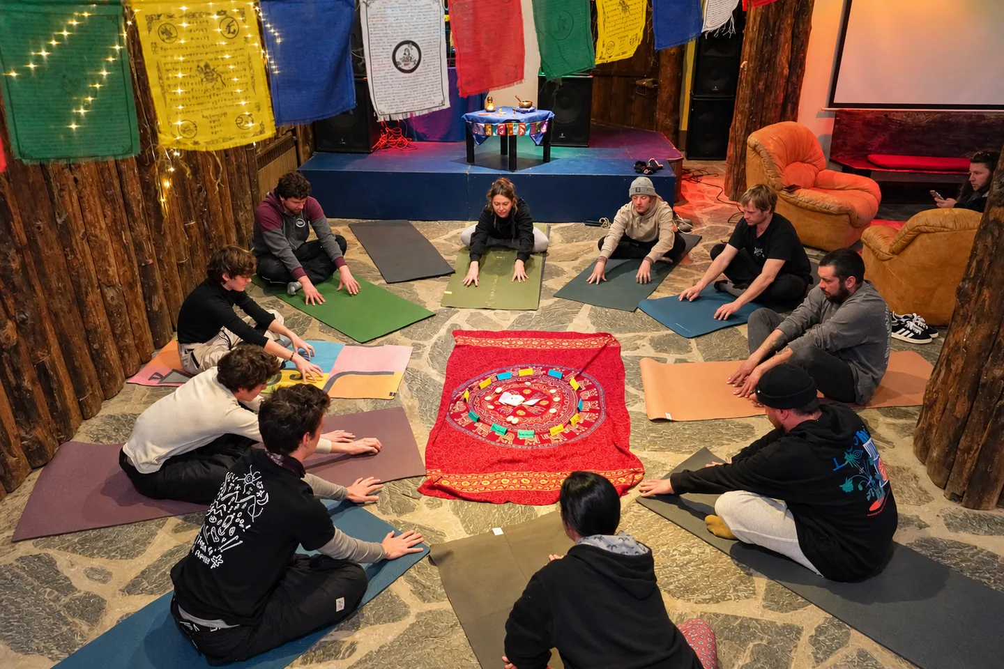 Grupo sentado en círculo alrededor de un mandala, bajo banderas tibetanas
